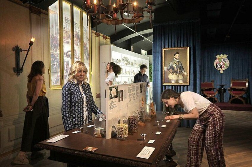 A museum exhibit with a table displaying artifacts, a framed portrait, and a chandelier. 5