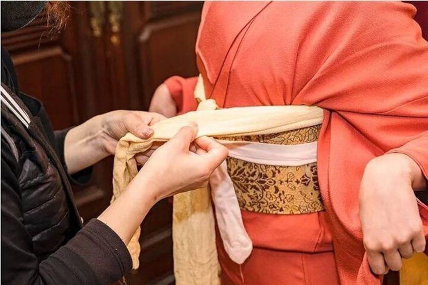 A person adjusting a sash on a traditional garment. 1