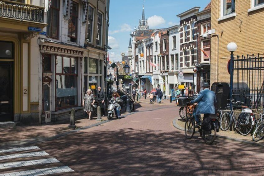 En brostensbelagt gade med historiske bygninger, et kirketårn i det fjerne og cykler parkeret langs fortovet. 3