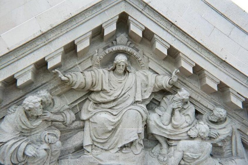 A stone relief sculpture with a central figure, flanked by two smaller figures, on a building facade. 5