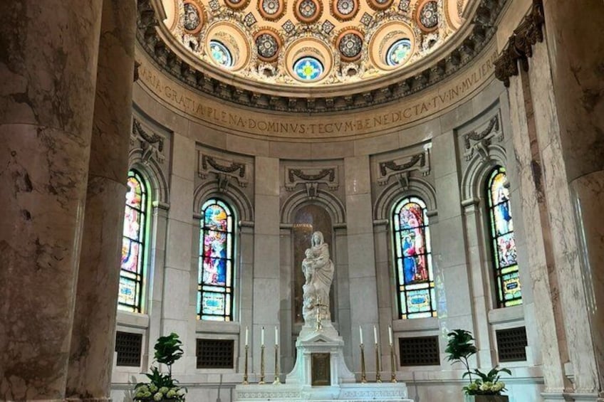 A grand hall with a central statue, ornate ceiling, and stained glass windows. 1