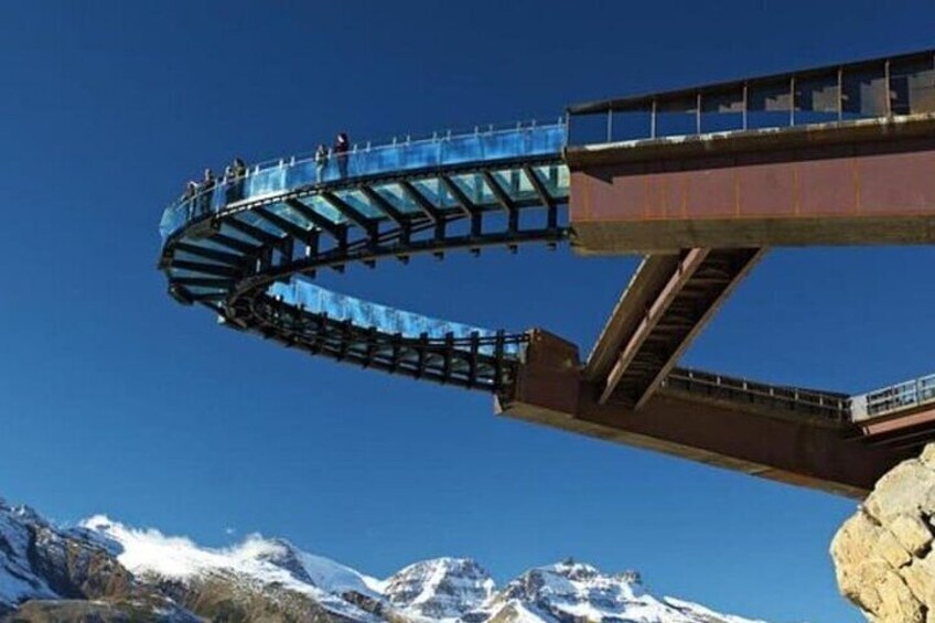 A roller coaster track with a glass bridge and a mountain backdrop. 1