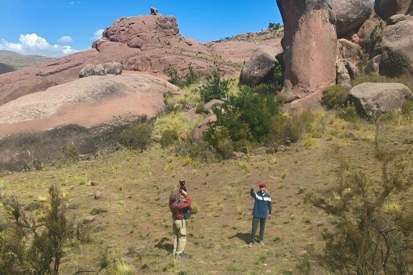 Two people hiking on a rocky terrain with large boulders and sparse vegetation. 3