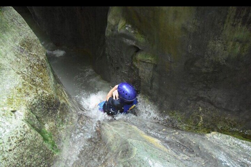 A person in a blue helmet navigating a narrow, rocky water channel. 3