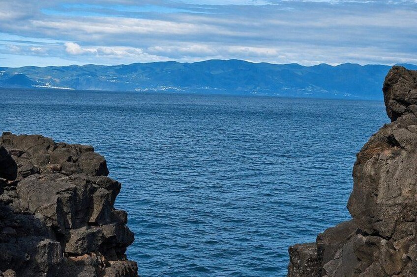 A rocky coastline with calm blue sea and distant mountains. 2