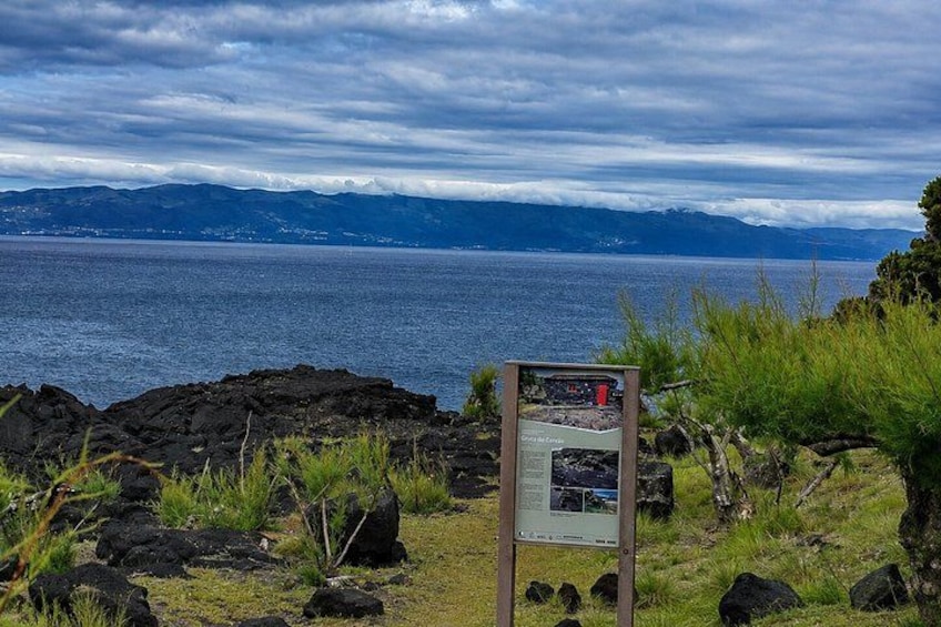 A coastal landscape with a rocky foreground, a signpost, and a view of the ocean and mountains in the distance. 4