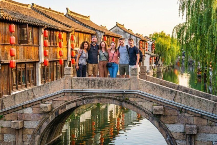 A group of people standing on a stone bridge over a canal with traditional wooden buildings and red lanterns. 1