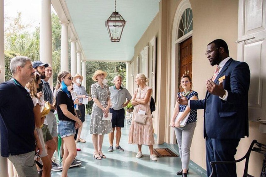 A group of people standing on a porch, some holding papers, with a man speaking to them. 4