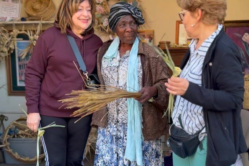 Three people holding dried plants, standing in front of a wall with various items displayed. 3