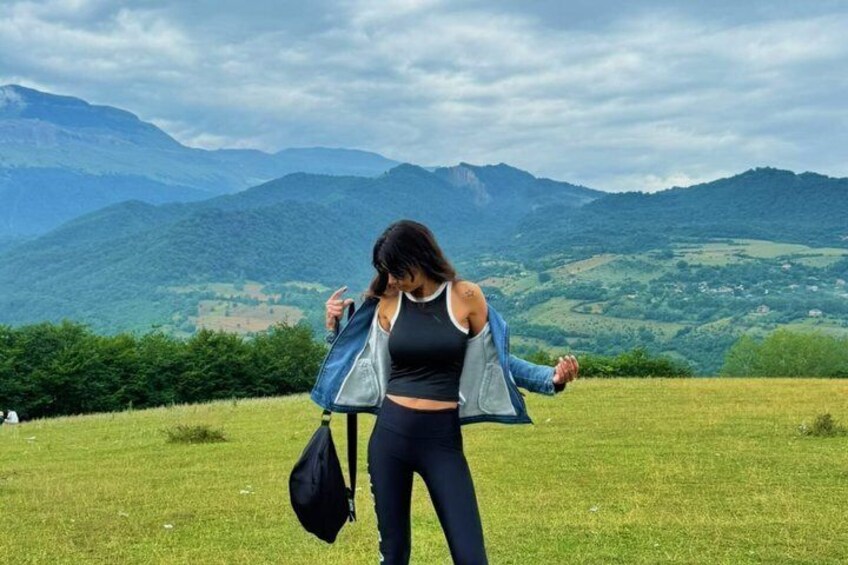 A person standing on a grassy field with a mountainous landscape in the background. 1