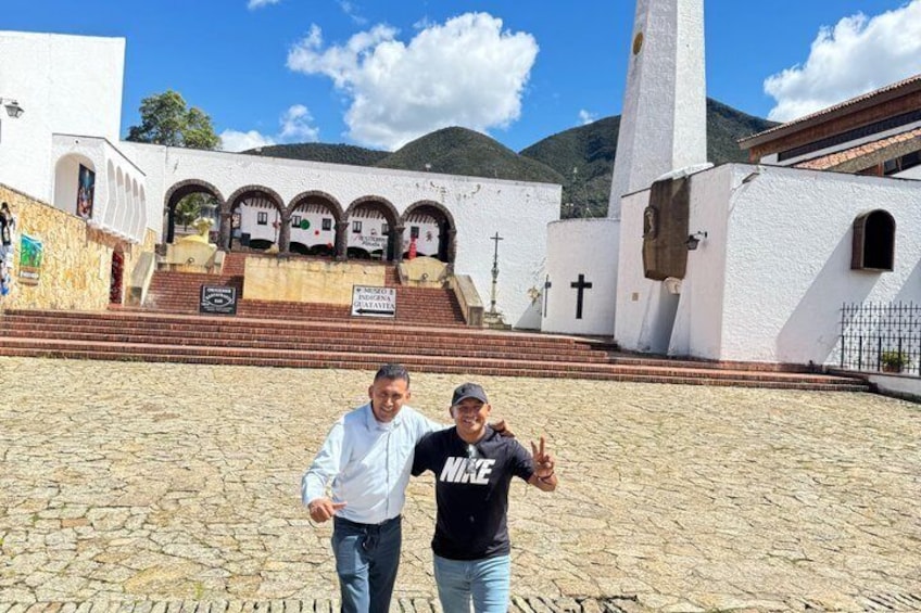 Two people standing in front of a church with a bell tower and steps leading up to it. 2