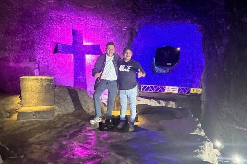Two people standing in a cave with a large cross and a blue-lit wall. 3