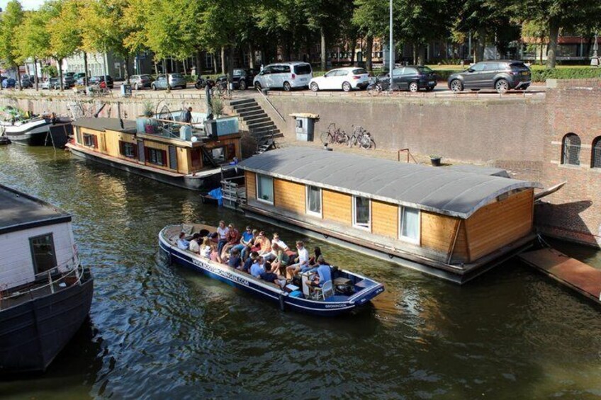 A houseboat with people on board, docked near a brick wall and a staircase. 1
