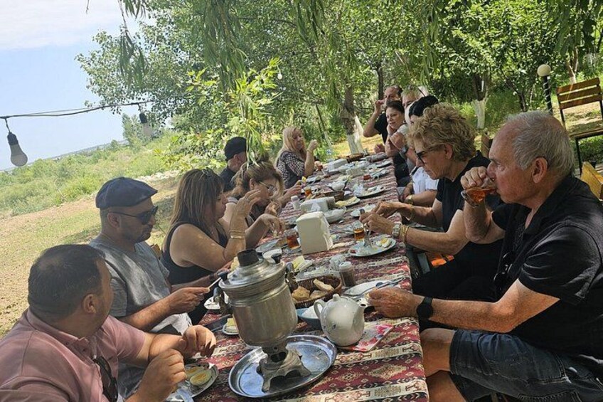A group of people sitting at a long table outdoors, eating and drinking. 4