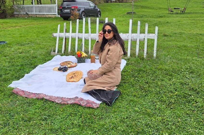 A person sitting on a blanket with food and drinks on a grassy field. 3