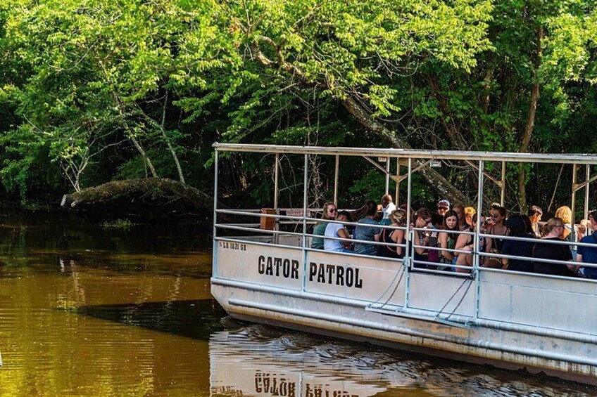 A boat named 'Gator Patrol' with passengers, surrounded by trees and water. 1