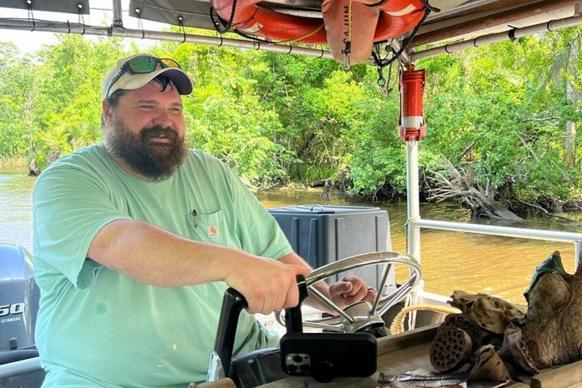 A person steering a boat on a river surrounded by greenery. 3