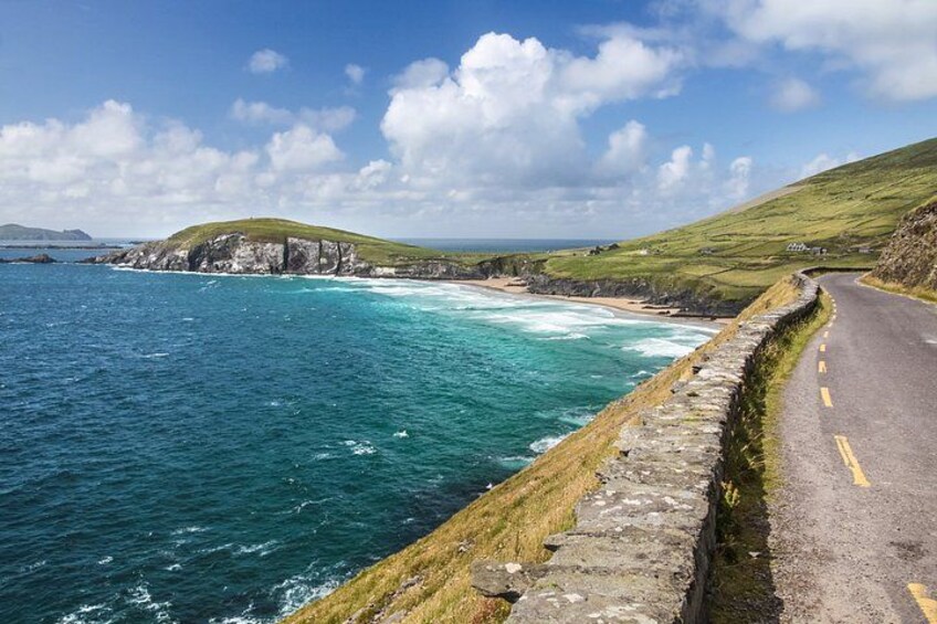 A coastal road with a stone wall, grassy hills, and the ocean. 4