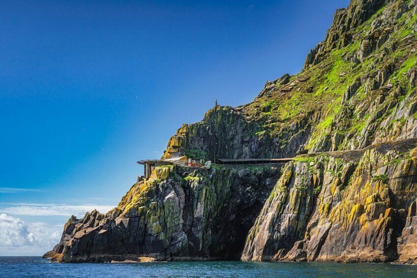 A coastal cliff with a narrow bridge and a small building. 3