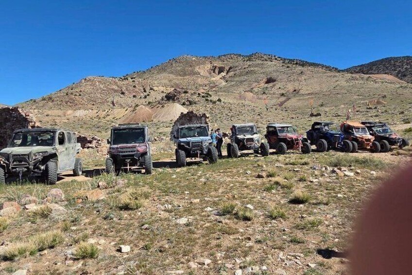 A line of off-road vehicles parked on a rocky hillside. 1