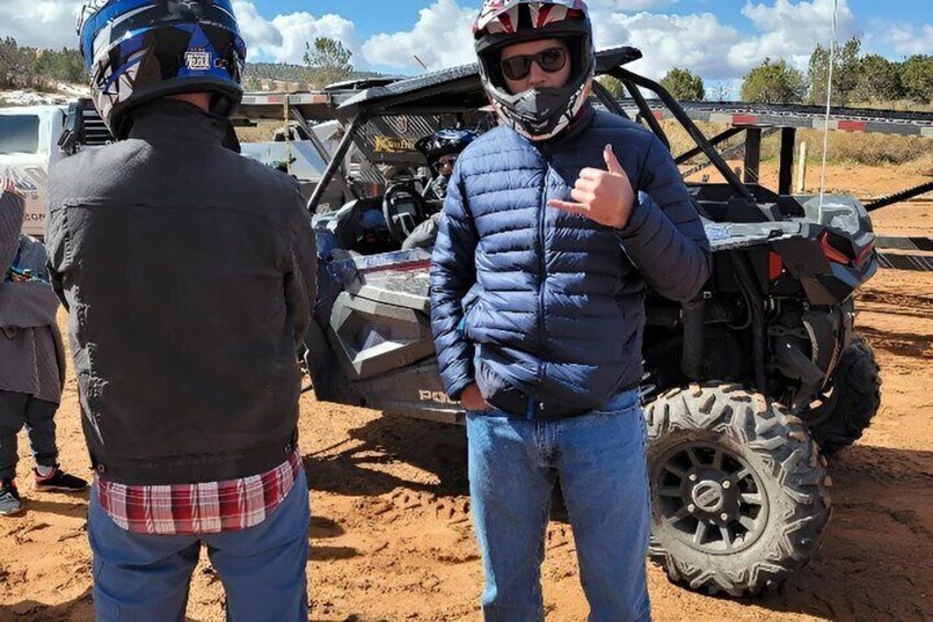 Two people standing near an off-road vehicle in a sandy area. 3