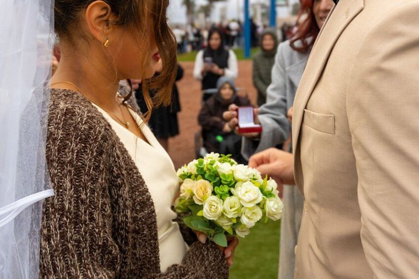 A person holding a bouquet of flowers, another person in a beige suit, and a crowd in the background. 5