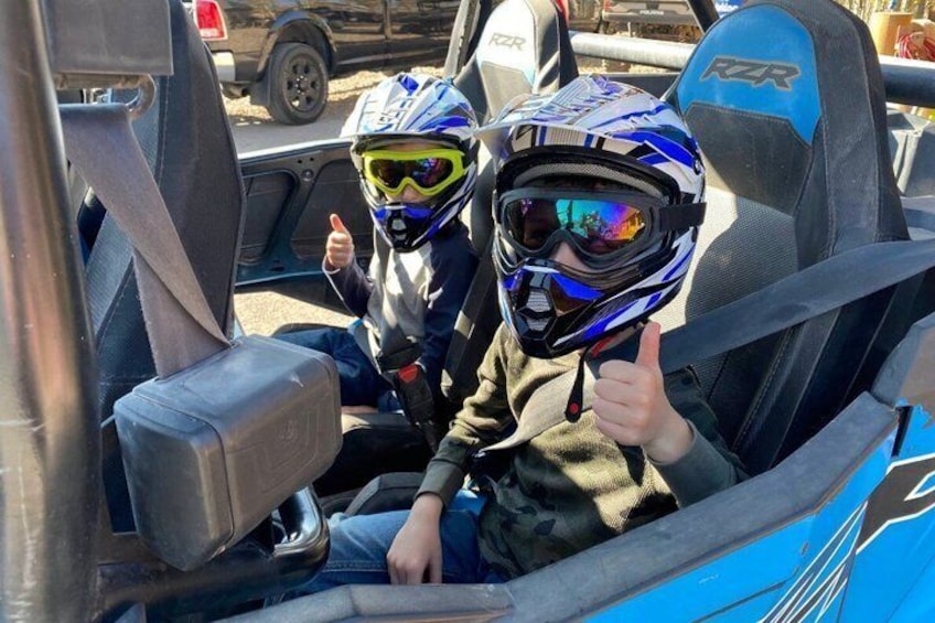 Two individuals in a vehicle with racing seats and helmets. 4