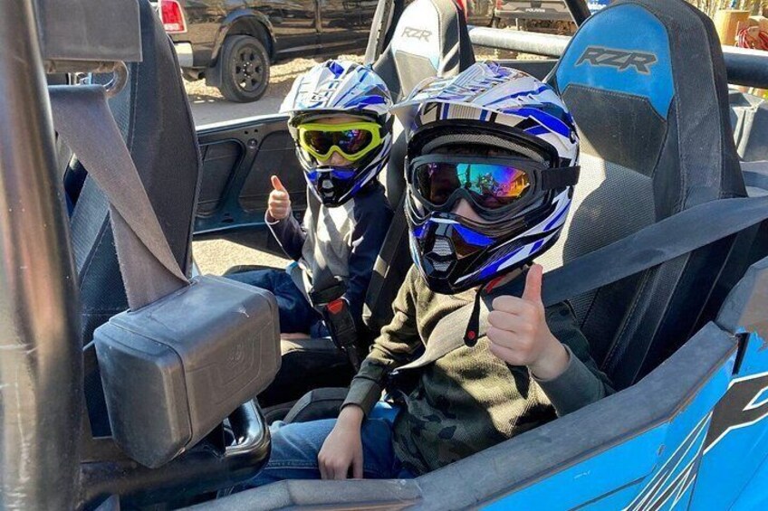 Two people in a vehicle wearing helmets and giving a thumbs up. 3
