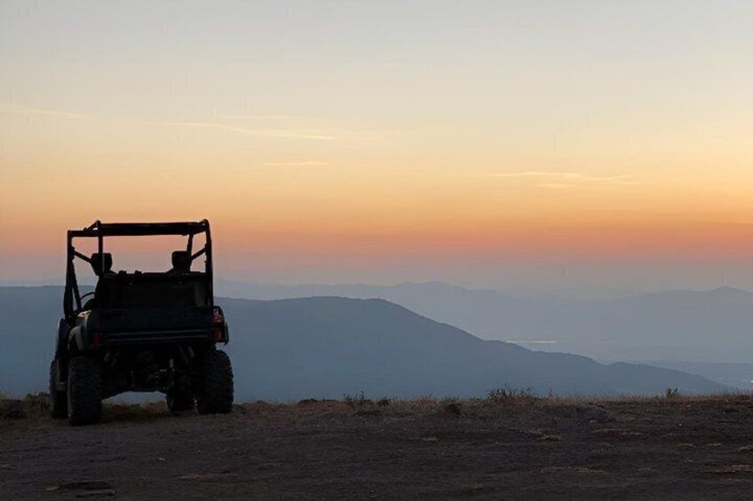 A vehicle parked on a hill with a sunset in the background. 4