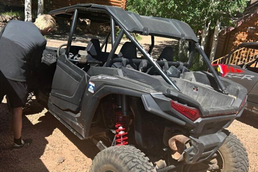 A black off-road vehicle with a visible logo, a person standing beside it, and a dirt ground. 1