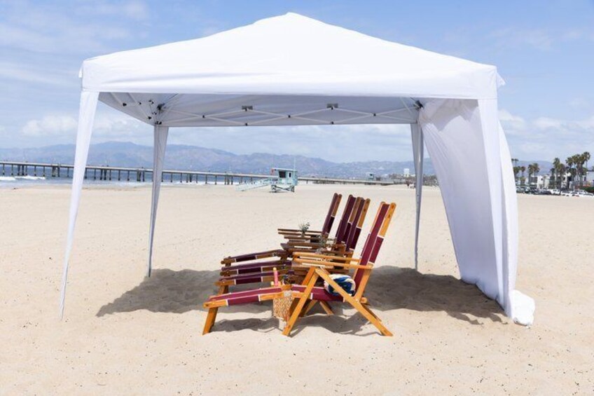 A beach with a white tent, beach chairs, and a wooden easel. 2