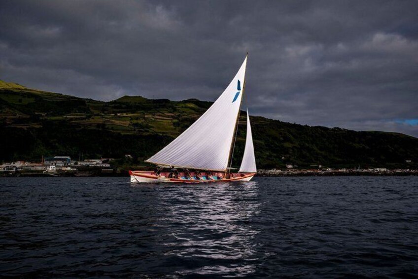 A sailboat with white sails on a body of water, with a hilly landscape in the background. 1