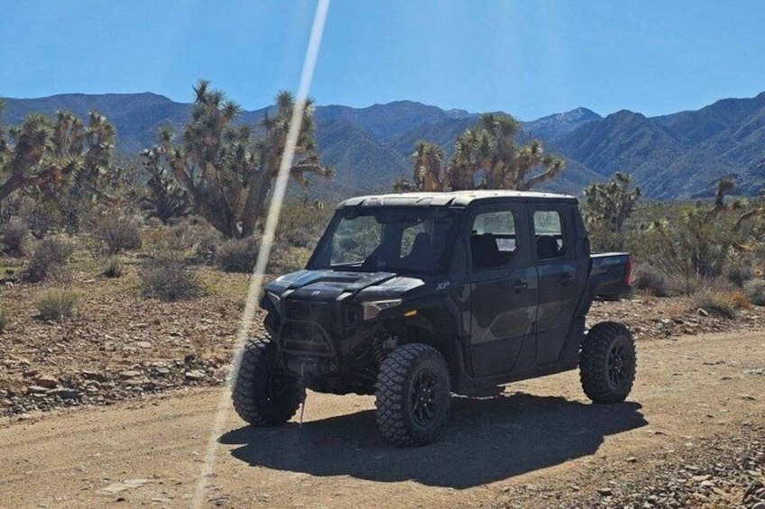 A black off-road vehicle parked on a dirt road with desert vegetation and mountains in the background. 1