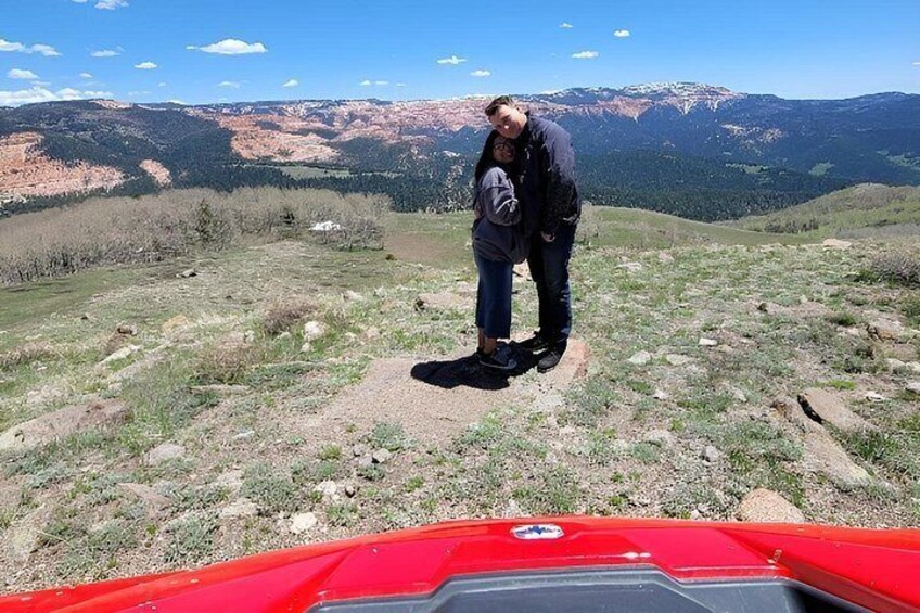 A person standing on a rocky outcrop with a mountainous landscape in the background. 3