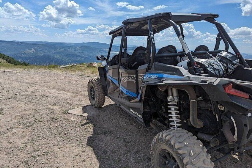 A Polaris RZR off-road vehicle parked on a dirt path with a mountainous landscape in the background. 2