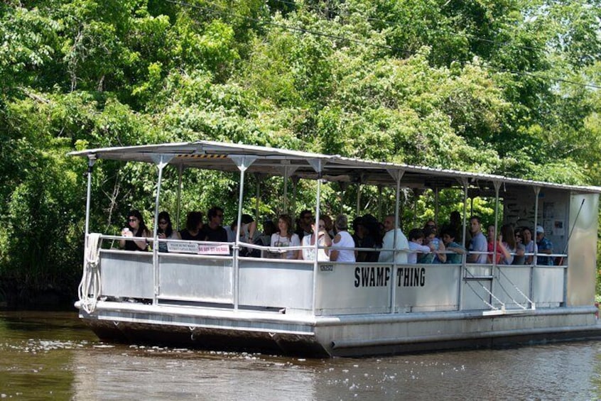 A boat named 'SWAMP THING' with passengers on a river surrounded by greenery. 1