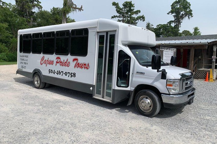 A white tour bus with 'Cajun Pride Tours' branding parked on gravel. 3