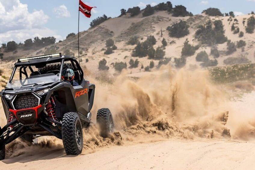 A red and black off-road vehicle driving through a sandy terrain with dust being kicked up. 3