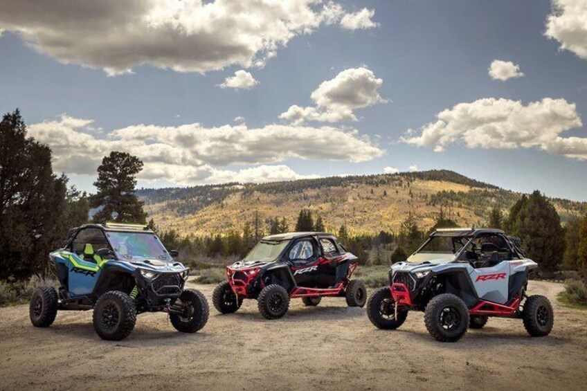 Three off-road vehicles parked on a dirt road with a mountainous landscape in the background. 1