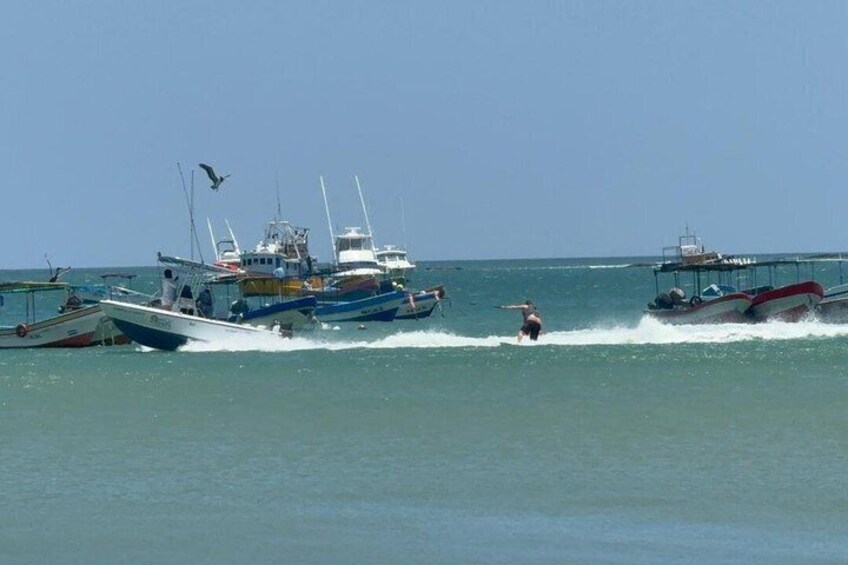 A person wakeboarding on a body of water with several boats and a clear sky in the background. 3