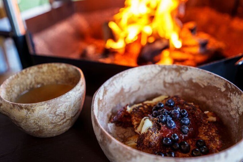A rustic setting with a fire in the background and two bowls, one with a dark substance and the other with a lighter one, possibly containing food or drink. 4