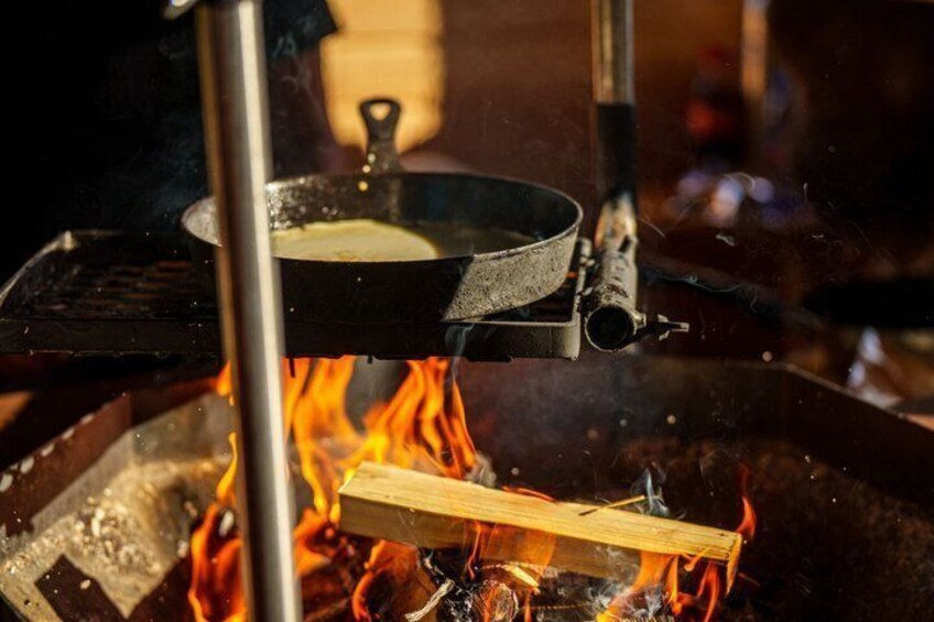 A cooking pan over an open flame with a piece of wood burning below. 5