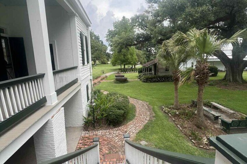 A white building with a balcony, a brick pathway, a palm tree, and a grassy area with a bench. 5