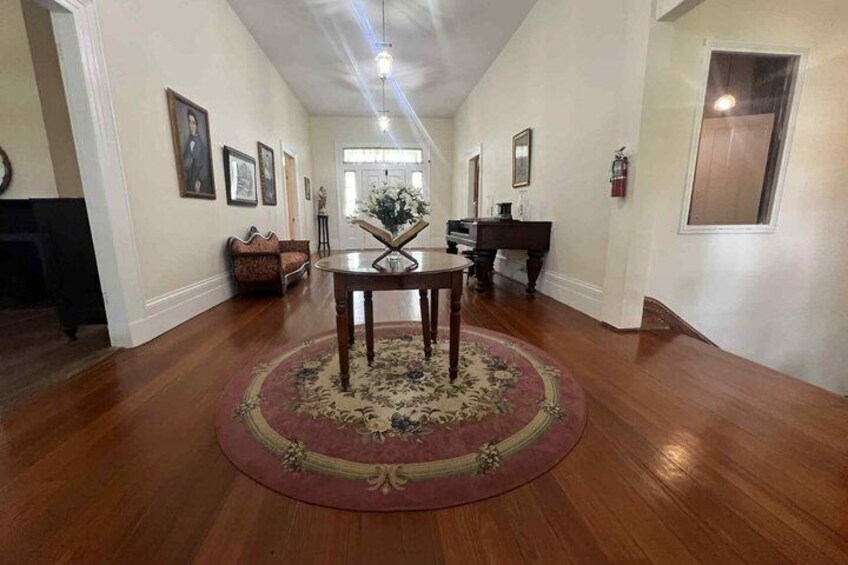 A hallway with wooden floors, a round rug, a piano, and framed pictures on the walls. 3