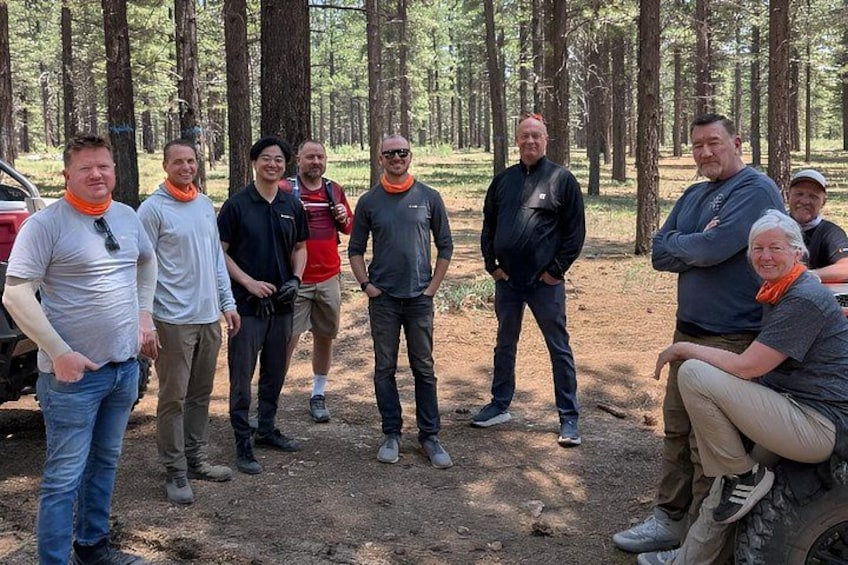 A group of people standing in a forested area with trees and a dirt ground. 5