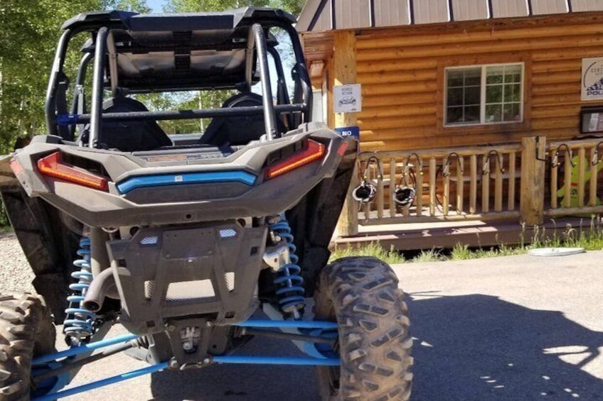 A Polaris RZR ATV parked in front of a wooden cabin with a porch. 2
