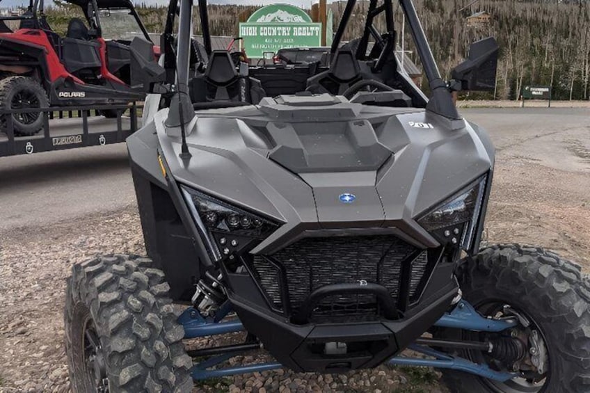 A Polaris ATV with a rugged front grille and large tires, parked on a gravel surface. 1