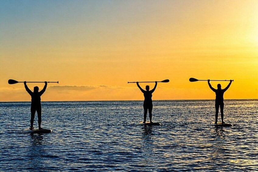 Three people standing on surfboards in the water, holding paddles above their heads. 5