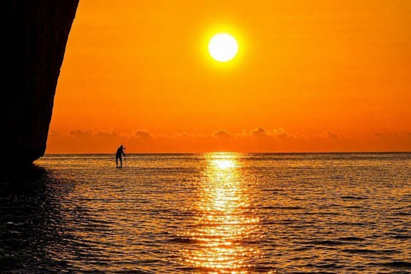 A sunset over the ocean with a person standing in the water. 2