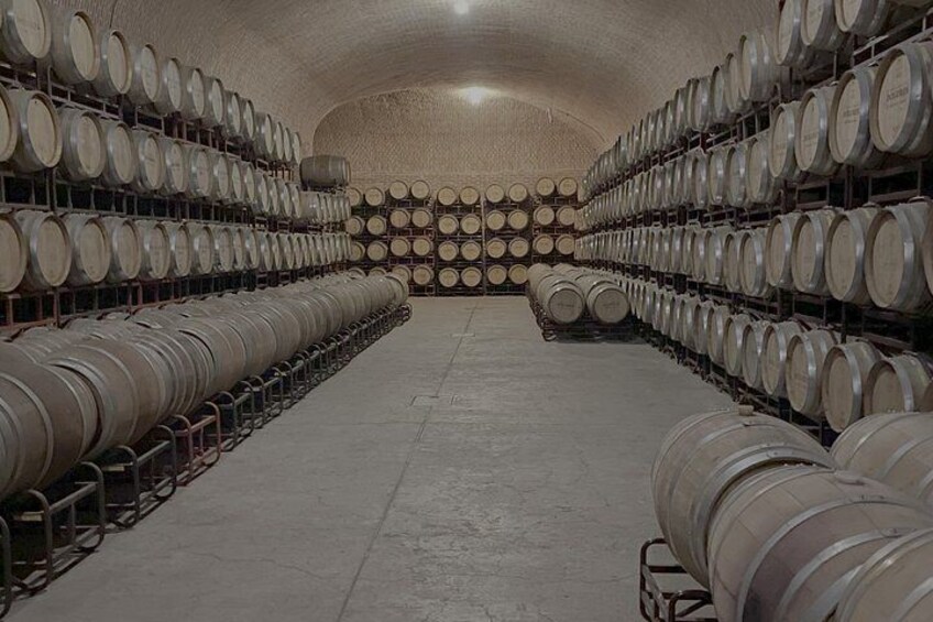 A large, dimly lit room with rows of wine barrels. 2